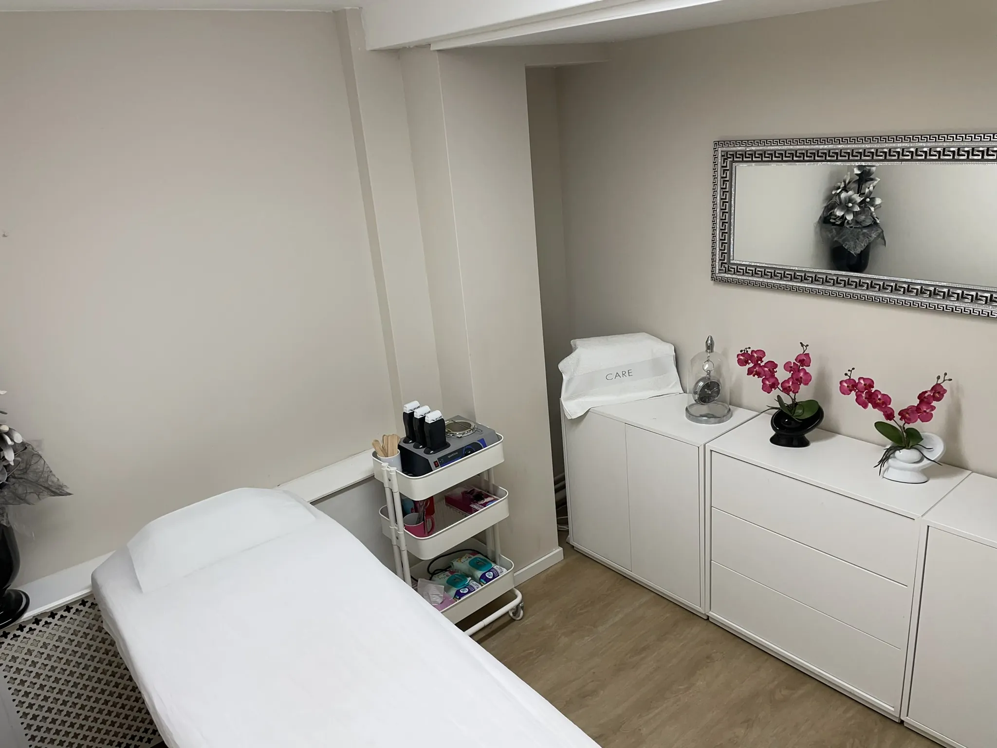 Lichte behandelkamer met behandelbank, orchideeën en een spiegel met zilveren lijst